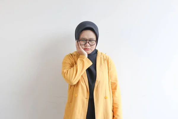 年轻美丽的亚洲穆斯林妇女 戴着眼镜 身穿黄色夹克 脸上挂着忧伤的表情 因为她的牙痛被白色的背景隔开了 — 图库照片