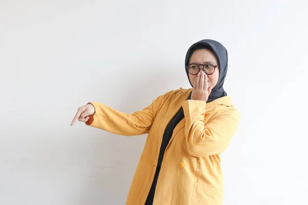 年轻美丽的亚洲穆斯林妇女 戴着眼镜 戴着黄色的夹克 手捂着嘴 另一只手指着被白色背景隔开的侧面 — 图库照片