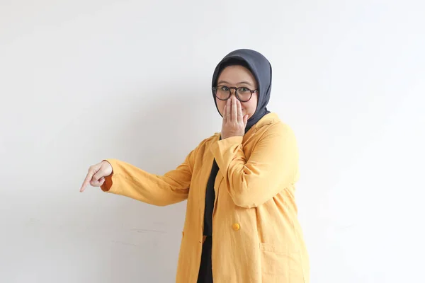 美しい若いアジア系イスラム教徒の女性 手で口をカバー眼鏡と黄色のブレザーを身に着けていると白の背景に横に隔離された他の手を指す — ストック写真