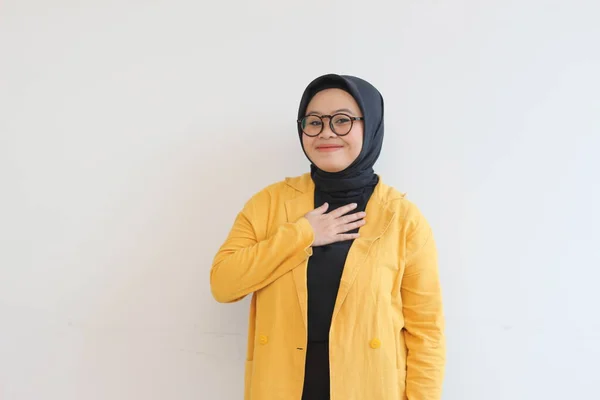 年轻美丽的亚洲穆斯林妇女 戴着眼镜 身穿黄色夹克 微笑着 手放在胸前 露出深情的姿态 与白色背景格格不入 — 图库照片