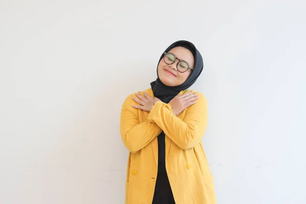 美しい若いアジア系ムスリム女性が眼鏡をかけ 黄色いブレザーの笑顔で両手を胸に置き 白い背景の上に孤立した愛情のジェスチャーを示す — ストック写真