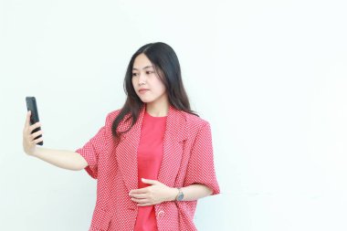 Güzel Asyalı bir kadının portresi. Kırmızı kıyafetler içinde. Elinde cep telefonu ve beyaz arka planda izole edilmiş bir gülümseme..