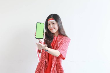 Endonezya 'nın bağımsızlık gününü kutlayan kırmızı kıyafetli güzel bir Asyalı kadının portresi. Elinde cep telefonu ve beyaz arka planda izole edilmiş bir gülümseme var..