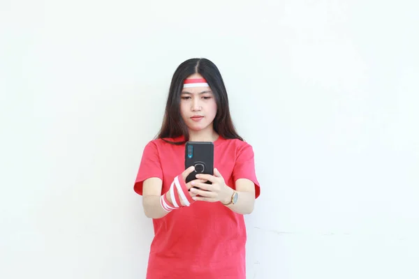 インドネシア独立記念日を祝う赤い衣装を着た美しいアジアの女性の肖像画は 白い背景に孤立した思考表現で携帯電話を保持しています — ストック写真