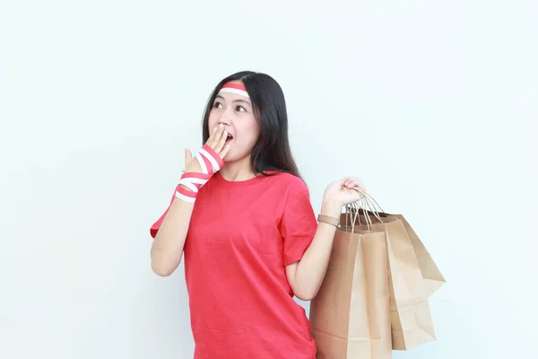 インドネシア独立記念日を祝う赤い衣装を着た美しいアジア人女性の肖像画 白い背景に隔離されたショッピングバッグをたくさん運ぶジェスチャー — ストック写真
