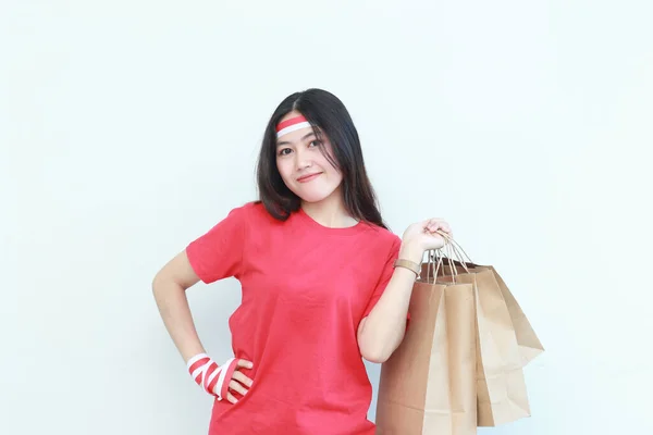 インドネシア独立記念日を祝う赤い衣装を着た美しいアジア人女性の肖像画 白い背景に隔離されたショッピングバッグをたくさん運ぶジェスチャー — ストック写真