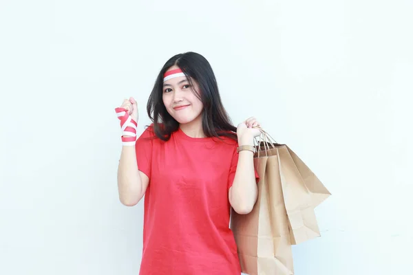 インドネシアの独立記念日を祝う赤い衣装を着た美しいアジア人女性の肖像画は 白い背景に隔離された幸せな表情でたくさんのショッピングバッグを運ぶジェスチャーによって — ストック写真