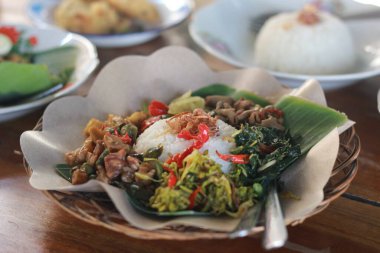 İçinde sotelenmiş papaya çiçekleri, tempeh, bağırsaklar, kasava yaprakları ve balkabağı var. muz yapraklarıyla servis edilir..