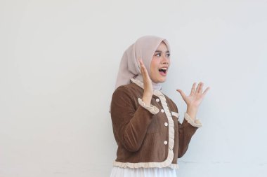 A young woman wearing a brown jacket and beige hijab is shown expressing surprise and excitement against a plain white background. clipart