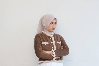 A young woman wearing a hijab stands with arms crossed, displaying a serious demeanor against a plain white backdrop. clipart