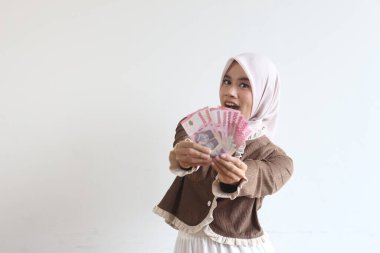 Tesettürlü neşeli bir Müslüman kadın Endonezya Rupia banknotları sergilerken gülümsüyor. Görüntü mutluluk ve finansal başarıyı iletir..