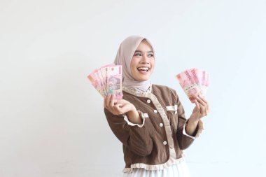 Bir tesettür içinde neşeli bir kadın Endonezya rupia banknotlarını mutlulukla sergiliyor, finansal başarı ve neşe hissini iletiyor.
