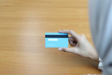 Bir el ahşap bir masanın üzerinde açık mavi bir kredi kartı tutar. Karta ve ele odaklan.. 