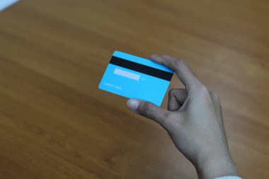 Birinin elinde açık mavi bir kredi kartı var. Kart ahşap bir yüzeyde duruyor..