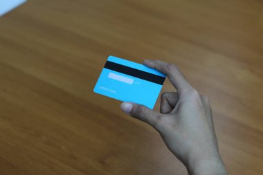 Bir insanın elinde açık mavi bir kredi kartı bulunur. Kart ahşap bir yüzeyde duruyor..