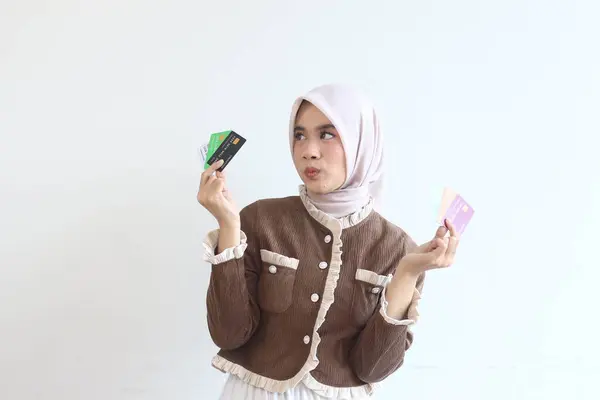 Tesettürlü genç bir kadın satın alma seçeneklerini göz önünde bulundurarak kredi kartlarını incelikle karşılaştırıyor. Finansal bir karar veriyor..