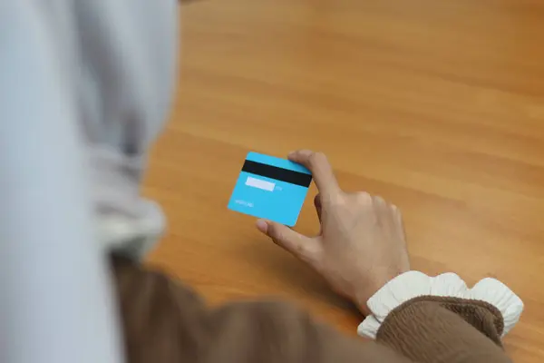 Açık mavi bir kredi kartı tutan bir kadın, çevrimiçi alışveriş veya finansal işlemleri öneriyor.
