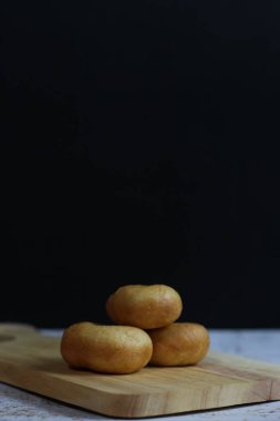 Üç altın-kahverengiye boyanmış mal, koyu bir arka planda, ahşap bir tahtanın üzerinde dinleniyor..