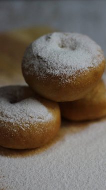 Cömertçe pudra şekerle kaplanmış birkaç çöreğin yakın çekimi. Resim, ikramların dokusunu ve rengini vurgular.