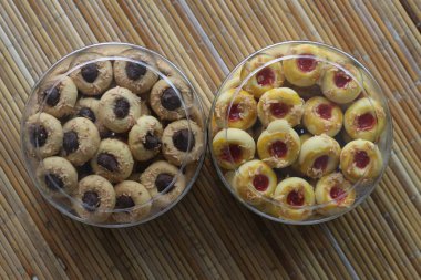 Çeşitli kurabiyelerle dolu iki kavanoz. Birinde çikolata, diğerinde çilek reçeli var. Bambu hasırında.