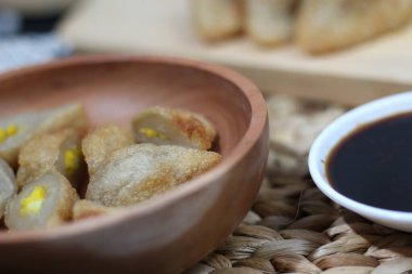 Popüler bir Endonezya balık keki olan Pempek 'in yakın çekimi, yanında koyu kahverengi bir sos ile ahşap bir kasede servis ediliyor. Çıtır çıtır ve parlak sarı yumurta dolgusu öne çıkıyor..