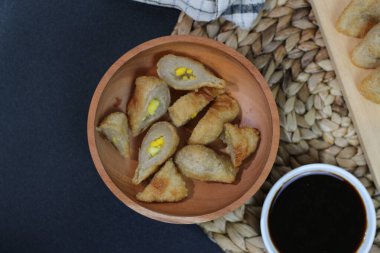 A wooden bowl filled with Pempek, a traditional Indonesian fish cake, served with a rich dark sauce. A truly delightful treat! clipart