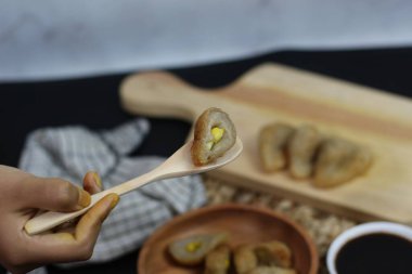 Bir Pempek 'in yakın çekimi, Endonezya' nın popüler balık keki, yumurta dolgusu görünür, tahta bir kaşıkta tutuluyor. Arka planda diğer Pempek var.
