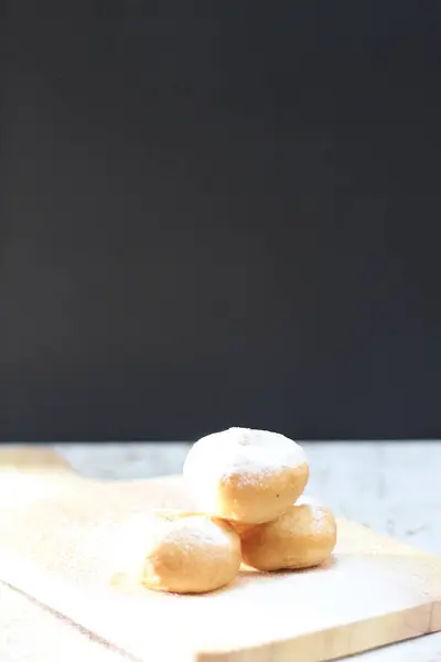 Tahta bir tahtanın üzerinde pudra şekerle kaplanmış üç altın esmer çörek resmi. Lezzetli ve cezbedici.