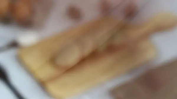 Odaklanamayan bir görüntü, ahşap bir kesim tahtası ve muhtemelen yeni pişirilmiş bir ekmek gösteriyor..