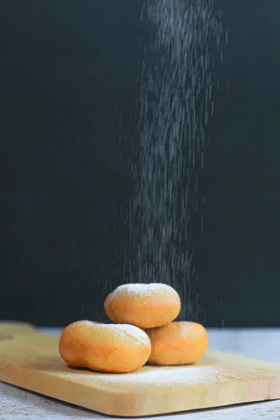 Tahtaya istiflenmiş üç altın esmer çörek, üzerine pudra şekeri dökülmüş..