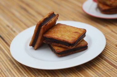 Tahta bir masada duran, beyaz bir tabağa istiflenmiş üç çikolata dolu kraker. Basit ama iştah açıcı bir görüntü..
