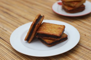 Üç çikolatalı sandviç krakeri beyaz bir tabakta, ahşap bir yüzeyde duruyor..