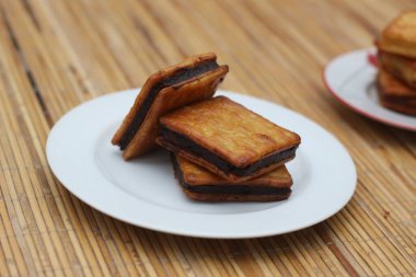 Tahta bir yüzey üzerinde durmakta olan, beyaz bir tabakta düzgünce istiflenmiş üç çikolata dolu kraker. Ne hoş bir sürpriz.!