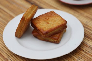 Three golden brown Kastengel cookies stacked on a white plate.  A delightful Indonesian treat. clipart