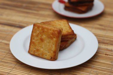 Beyaz bir tabağa düzgünce istiflenmiş, ahşap bir yüzeye yerleştirilmiş üç altın kahverengi kraker yakın plan..