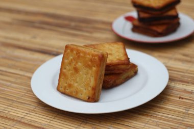 Tahta bir yüzey üzerinde beyaz bir tabağa istiflenmiş üç çıtır kraker..