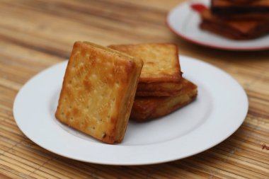 Beyaz bir tabağa düzgünce istiflenmiş üç tane altın sarısı kraker. Krakerler çıtır çıtır ve çok iştah açıcı görünüyor..
