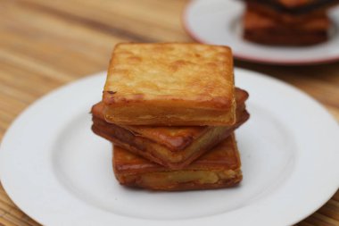 Beyaz bir tabağa düzgünce istiflenmiş üç altın sarısı krakerin yakın plan çekimi. Krakerlerin çıtır çıtır bir dokusu var ve lezzetli görünüyor..