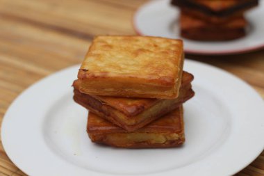 Üç altın sarısı kraker saf beyaz bir tabağa istiflenmiş, açık kahverengi ahşap bir yüzey üzerinde duruyor..