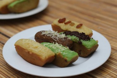 A plate of assorted Indonesian kuih, featuring various flavors and toppings like raisins, chocolate, and cheese.  A delightful culinary treat! clipart