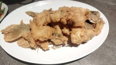 Beyaz oval tabakta servis edilen kızarmış balık. İştah açıcı ve altın rengi kahverengi.