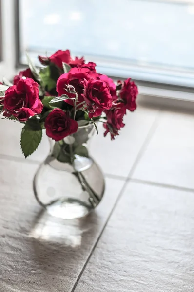 Bouquet of garden roses in a transparent glass vase with water on the ceramic tile of the floor.