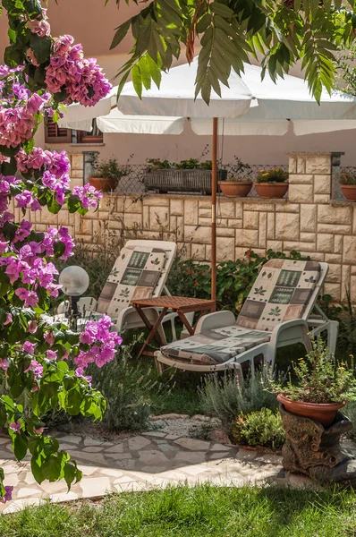 A small courtyard with flowering plants, lawn, sun beds and an umbrella in private possession on the Adriatic in Croatia.