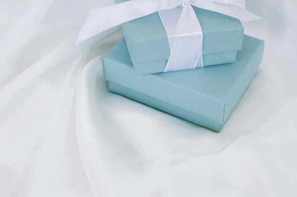 Turquoise boxes for the jewelry with white silk ribbon on the white silk background.