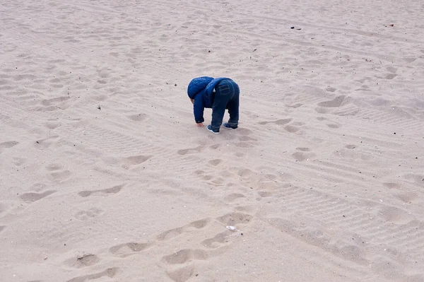Soğuk bir günde kumsalda oynayan tatlı bir çocuk.