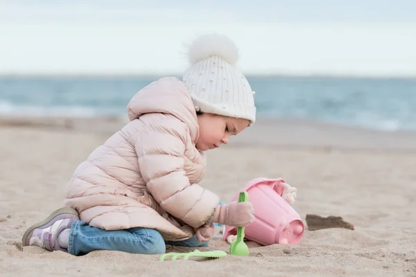 stock image Little girl is digging in the sand on a cold day at the beach