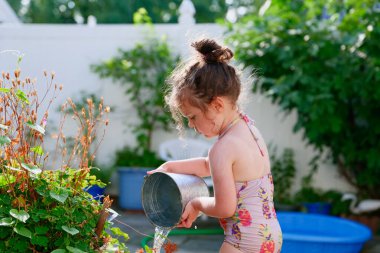 Bahçede bir yaz günü bitkileri kovayla sulayan tatlı bir genç kız.