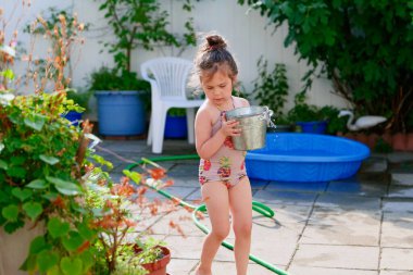 Bahçede bir yaz günü bitkileri kovayla sulayan tatlı bir genç kız.