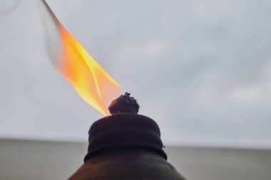 Alevler ve yanan fitil, bulutlu bir gökyüzüne karşı bir yağ meşalesinde