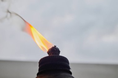 Alevler ve yanan fitil, bulutlu bir gökyüzüne karşı bir yağ meşalesinde